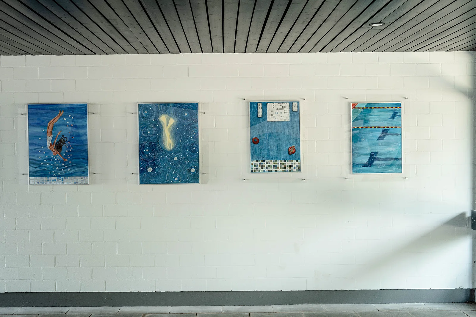 Mehrere Kunstwerke an einer weißen Wand im Freibad